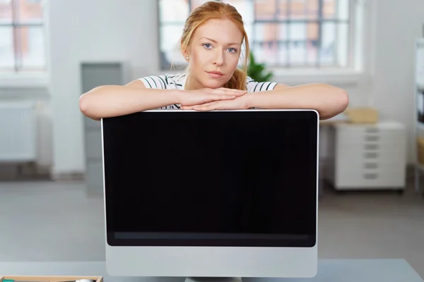 Mujer joven seria apoyada en un monitor de escritorio — Foto de Stock