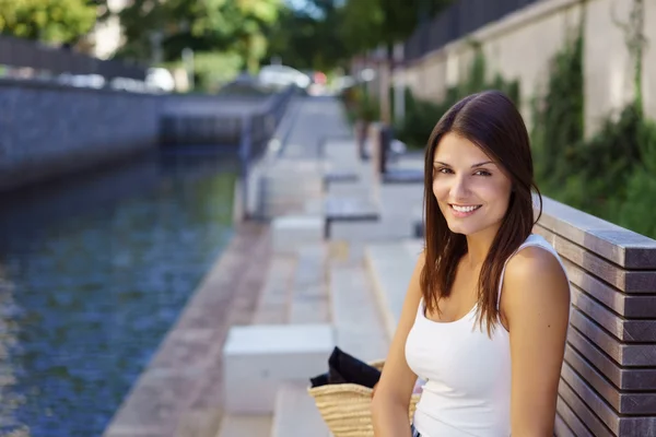 Mujer sonriente sentada en el banco cerca de la vía navegable — Foto de Stock