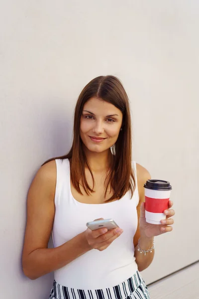 Mujer joven con café y teléfono apoyado en la pared — Foto de Stock