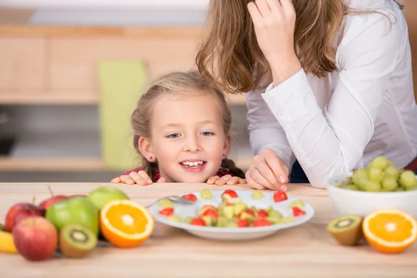 Chica mirando ensalada de frutas en la cocina — Foto de Stock