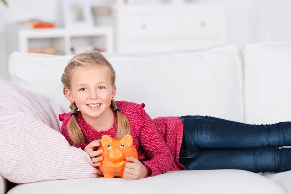 Menina no sofá segurando banco porquinho — Fotografia de Stock