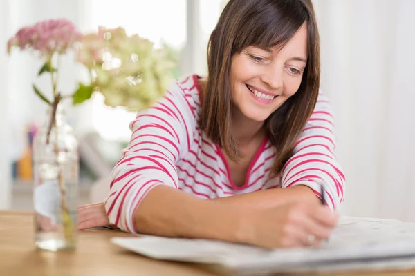 Mujer sonriendo mientras escribe en un periódico — Foto de Stock