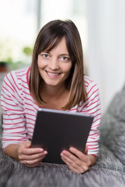 Donna sorridente sdraiata su un divano con il suo tablet — Foto Stock