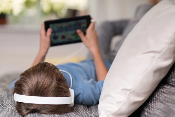 Young boy lying listening to music on his tablet — Stock Photo, Image