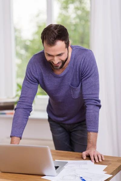 Uomo sorridente mentre legge un messaggio sul suo computer portatile — Foto Stock