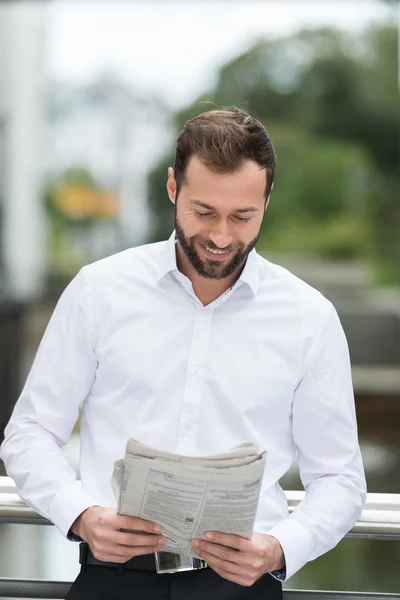 Uomo sorridente mentre legge il giornale all'aperto — Foto Stock