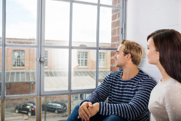 Couple sitting looking out of an urban apartment — Stock Photo, Image