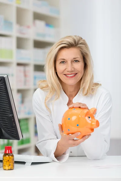 Female pharmacist with piggy bank — Stock Photo, Image