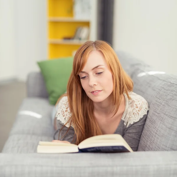 Mujer acostada en un sofá mientras lee un libro —  Fotos de Stock