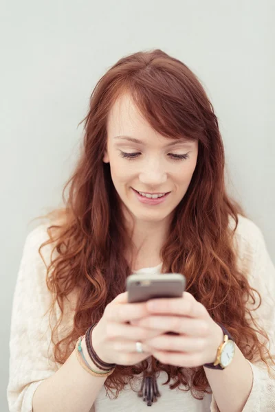 Mujer joven sonriendo mientras usa un teléfono inteligente — Foto de Stock