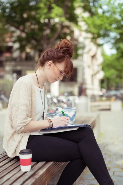Young woman sitting on a park bench working — Stock Photo, Image