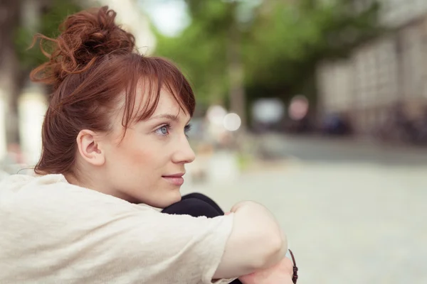 Thoughtful young woman sitting hugging her knees — Stockfoto