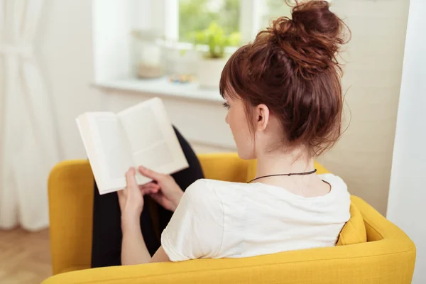 Jovem mulher lendo um livro enquanto sentado na cadeira — Fotografia de Stock