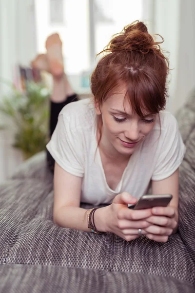 Girl with Phone Lying on her Stomach on Couch — Stock Photo, Image