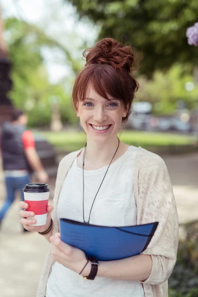 Pretty young woman carrying coffee and a file — Stock Photo, Image