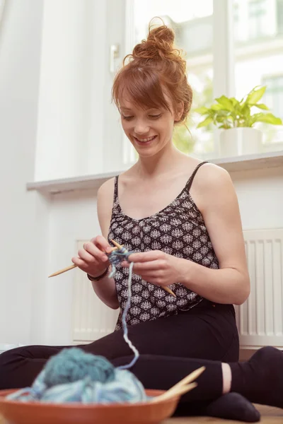 Sorridente giovane donna seduta a maglia — Foto Stock