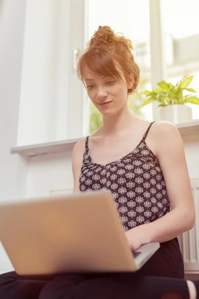 Νεαρή γυναίκα συνεδρίασης πληκτρολογώντας σε ένα φορητό υπολογιστή — Φωτογραφία Αρχείου
