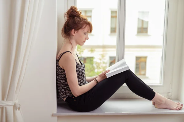 Ładna kobieta, czytając książkę na parapecie — Zdjęcie stockowe