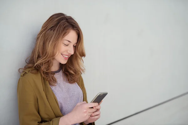 Hübsches Mädchen, das ihr Handy benutzt, während es sich an die Wand lehnt — Stockfoto