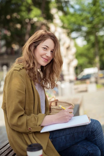 Jolie fille souriante avec stylo et notes au banc — Photo