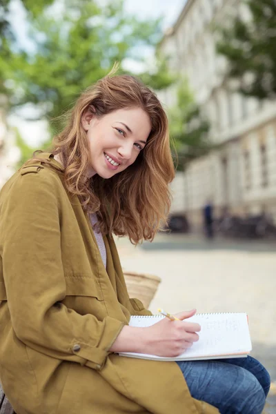 Lächelndes Schulmädchen auf Bank mit Stift und Notizen — Stockfoto