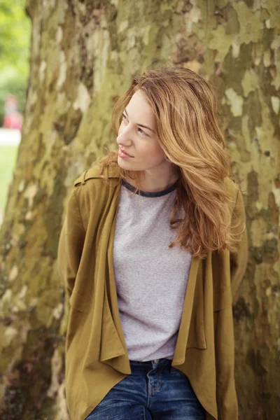 Pensativo joven dama en el árbol tronco mirando hacia arriba — Foto de Stock