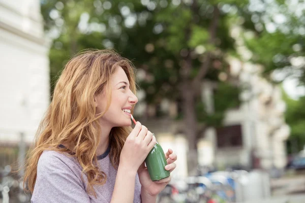 Glückliches blondes Mädchen trinkt eine Flasche grünen Saft — Stockfoto