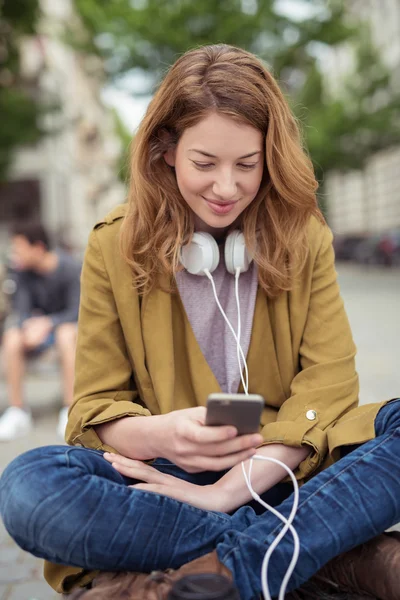 Szczęśliwa dziewczyna siedzi na ławce przeglądania na jej telefon — Zdjęcie stockowe