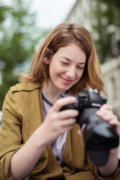 Chica rubia sonriendo mientras mira fotos en DSLR — Foto de Stock