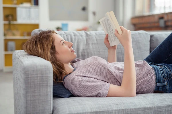 Mujer joven relajante con libro sobre sofá —  Fotos de Stock