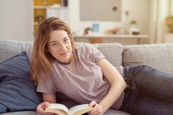 Jovem deitada em um sofá com um livro — Fotografia de Stock