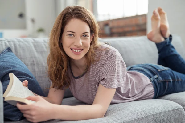 Teen Girl with Book Lying on her Stomach on Couch — Stock Photo, Image