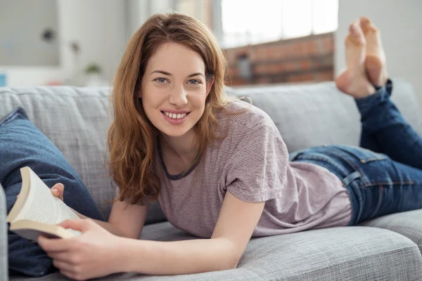 Teen Girl with Book Lying on her Stomach on Couch — Stock Fotó