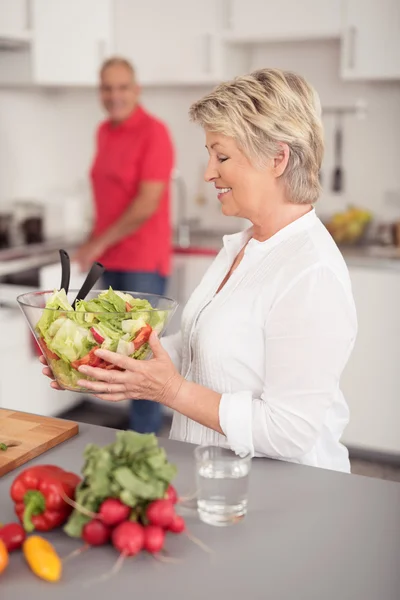 Feliz esposa sosteniendo ensalada fresca en la cocina — Foto de Stock