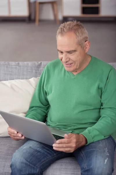 Мужчина средних лет сидит на диване с ноутбуком — стоковое фото