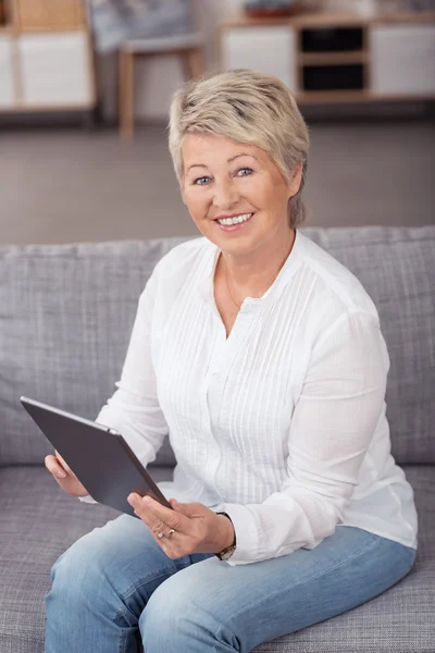 Middle Aged Woman At the Couch with Tablet — Stockfoto