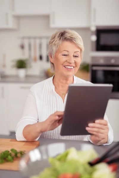 Mujer de mediana edad feliz con la tableta en la cocina —  Fotos de Stock