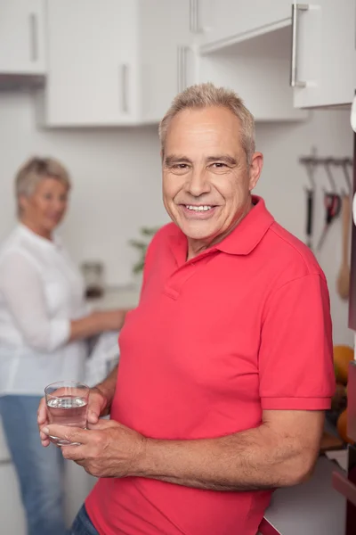 Homme âgé tenant un verre d'eau à la cuisine — Photo