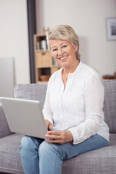 Felice donna di mezza età con computer portatile sul divano — Foto Stock