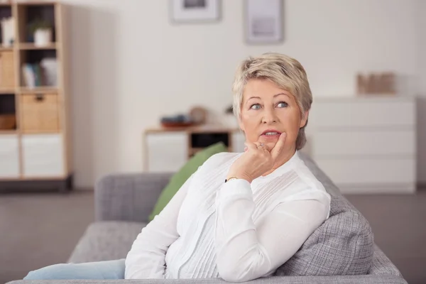 Nachdenkliche Frau mittleren Alters sitzt auf der Couch — Stockfoto