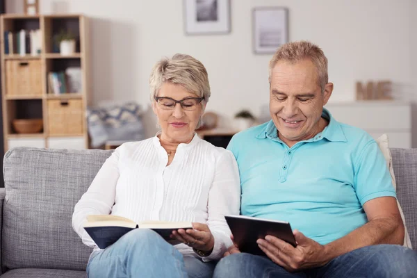 Leitura de casal de meia-idade com livro e tablet — Fotografia de Stock