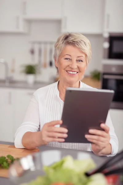 Heureuse femme âgée tenant une tablette à la cuisine — Photo