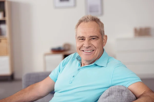 Senior entspannt auf der Couch und lächelt in die Kamera — Stockfoto