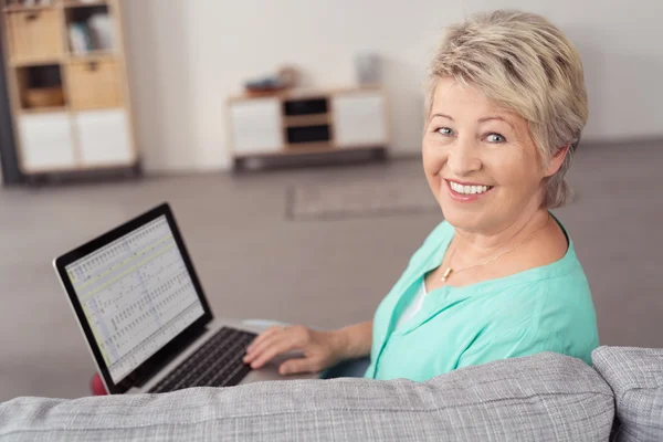 Mujer mayor alegre en el sofá con el ordenador portátil —  Fotos de Stock