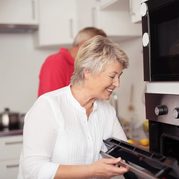 Happy Matured Housewife Cooking Something in Oven — Stock fotografie