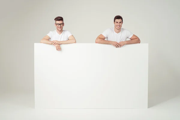 Веселые мужчины, опирающиеся на пустую белую доску — стоковое фото