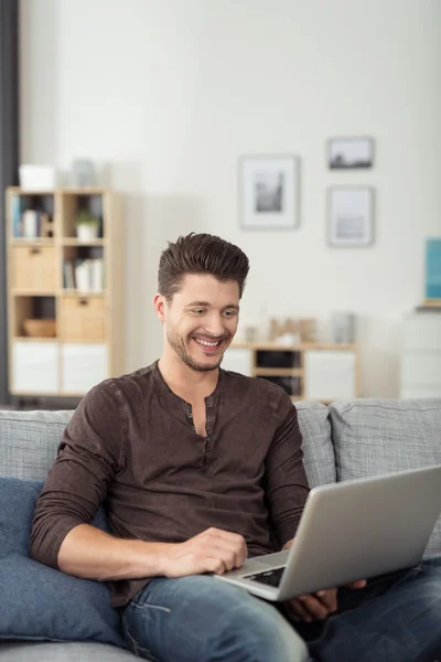 Jeune homme heureux avec ordinateur portable assis sur le canapé — Photo