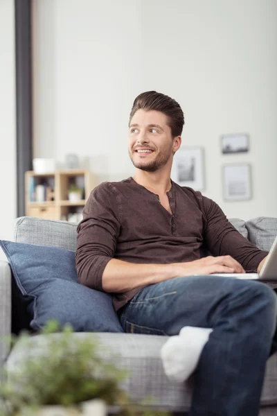 Smiling Young Man on Couch Looking Into Distance — Stok fotoğraf