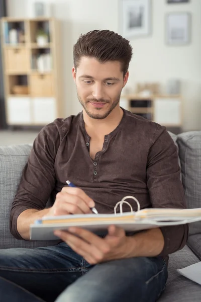 Bel ragazzo che scrive sui suoi appunti sul divano — Foto Stock