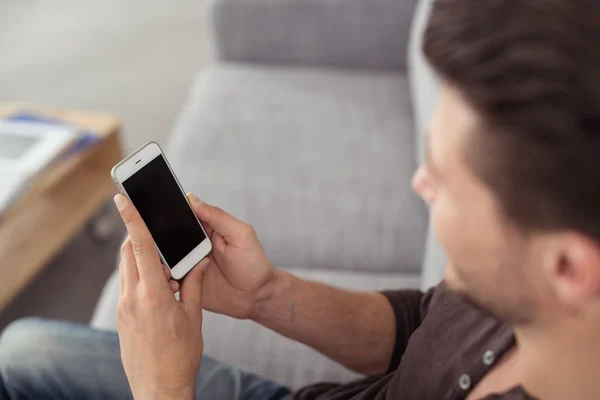 Jeune homme au canapé tenant son téléphone portable — Photo